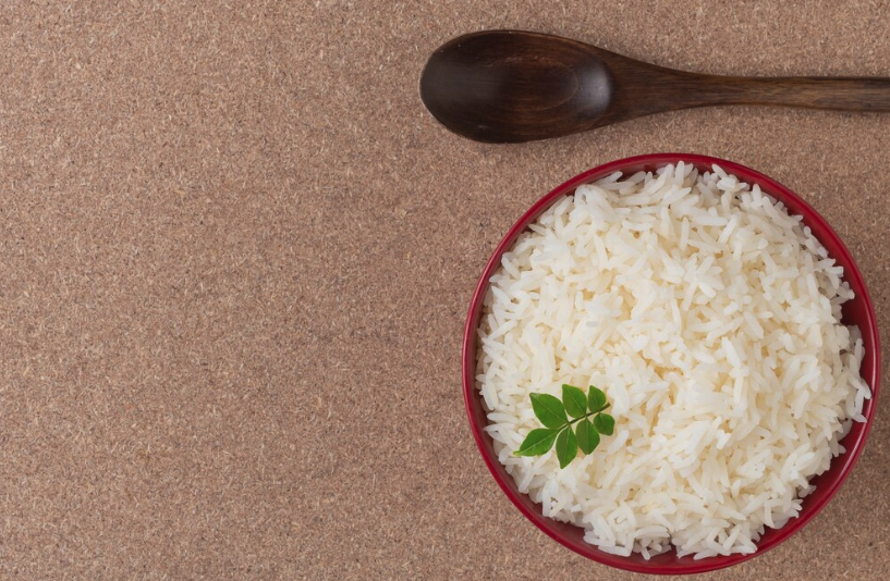 Tigela de arroz branco soltinho com folha de salsa, ao lado de uma colher de madeira.

