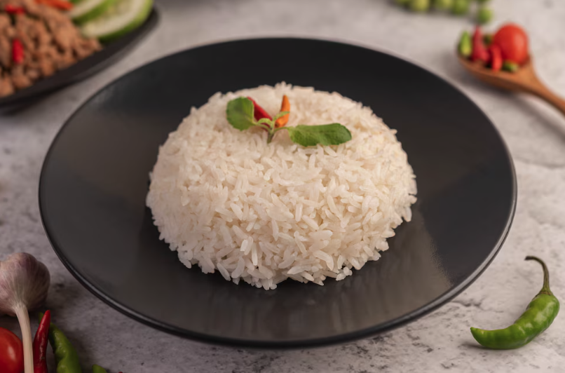 Porção de arroz branco soltinho decorado com ervas, servido em um prato preto.

