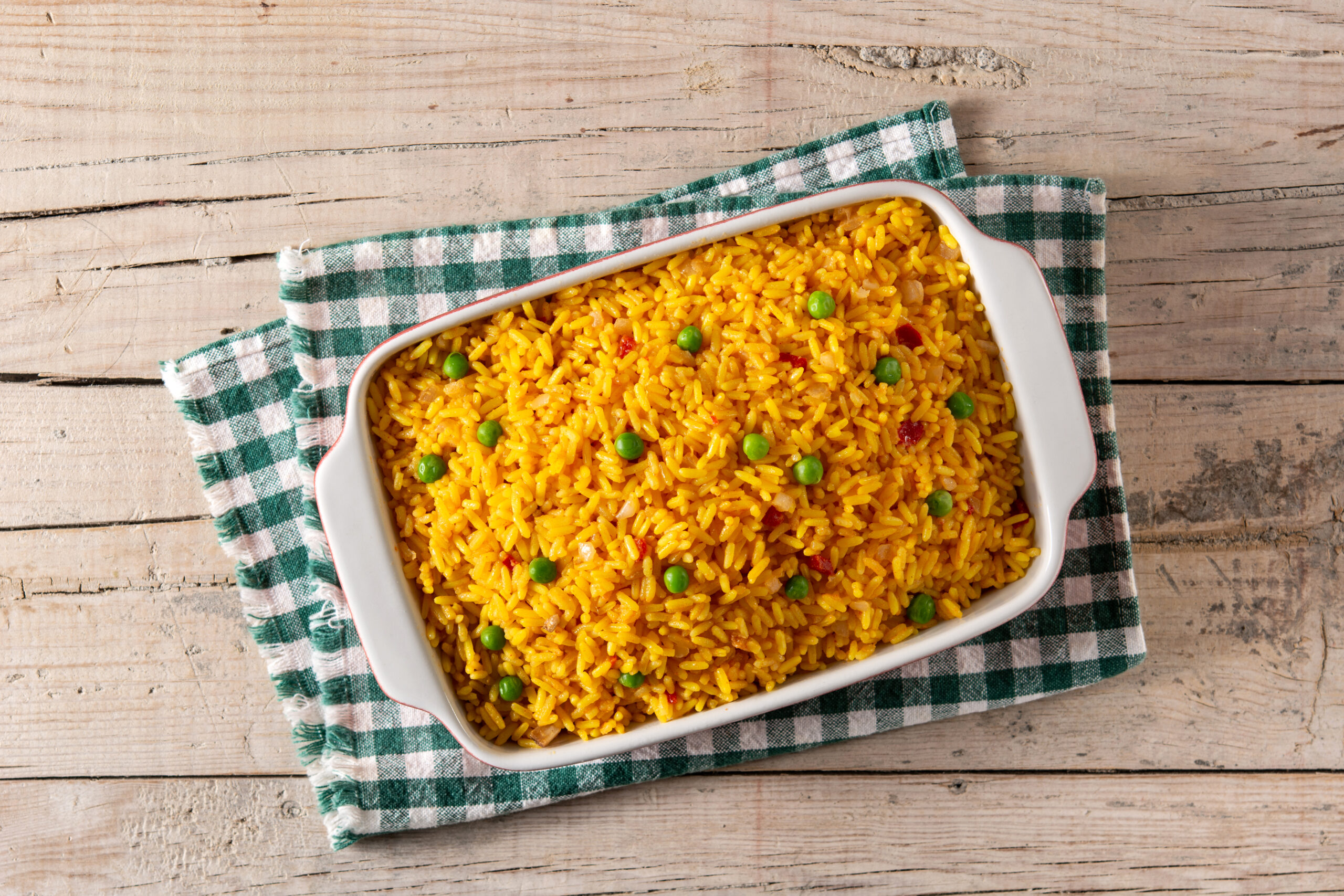 Travessa de arroz de forno com ervilhas, sobre um pano xadrez verde e branco.