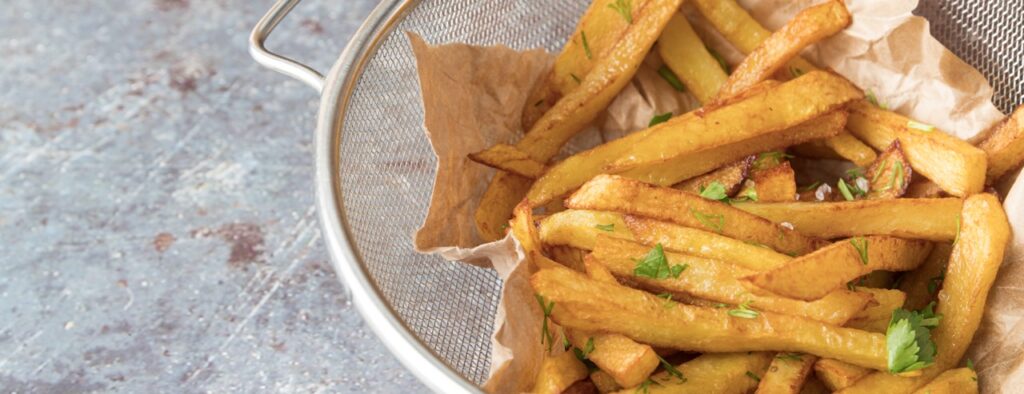 Batata frita feita em air fryer saudável, servida em um pote de metal com salsa em cima