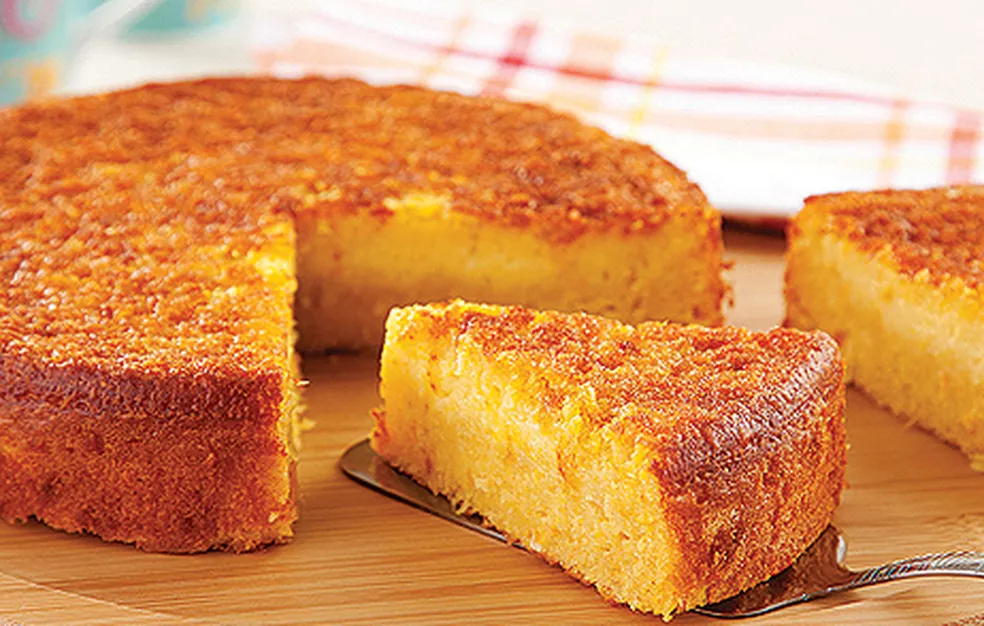 Fatia de bolo de milho cremoso sendo servida, com textura dourada e crocante.