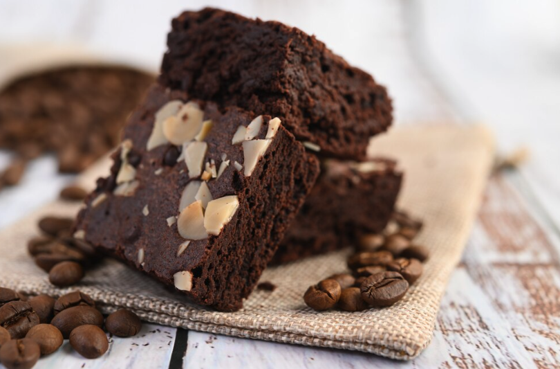 Brownies de chocolate com amêndoas, servidos sobre uma superfície rústica ao lado de grãos de café.