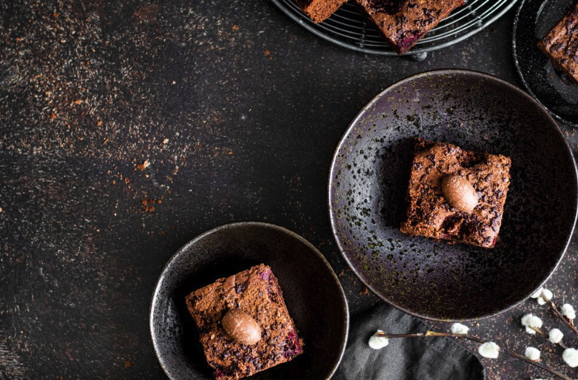 Brownies de chocolate servidos em tigelas escuras, decorados com pequenos chocolates sobre uma superfície rústica.

