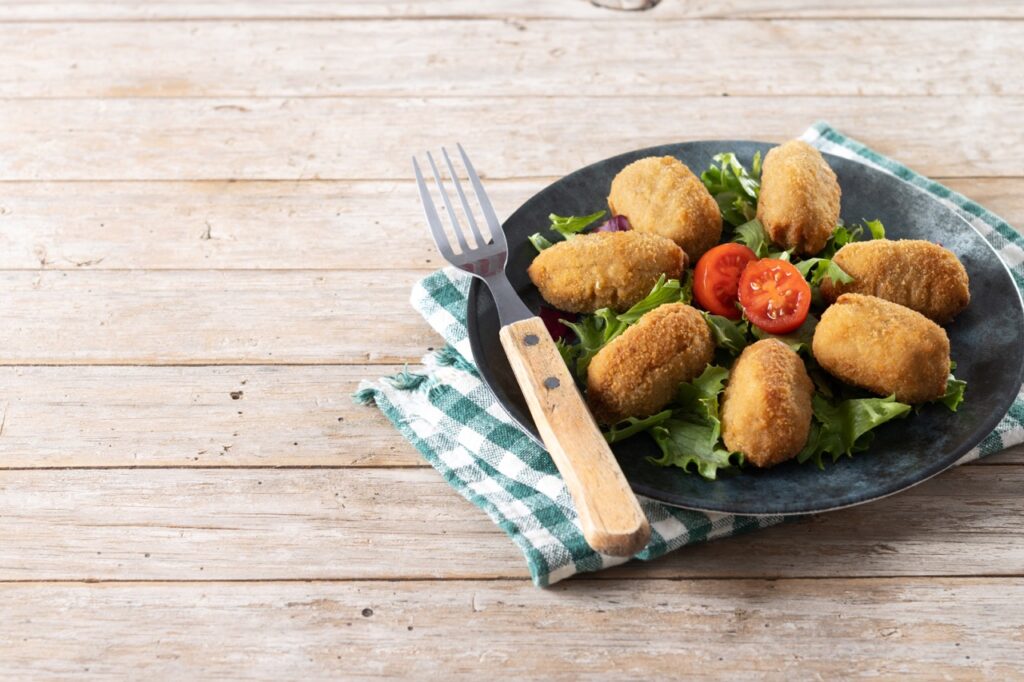 Coxinhas de frango empanadas servidas em um prato com folhas verdes e tomate.