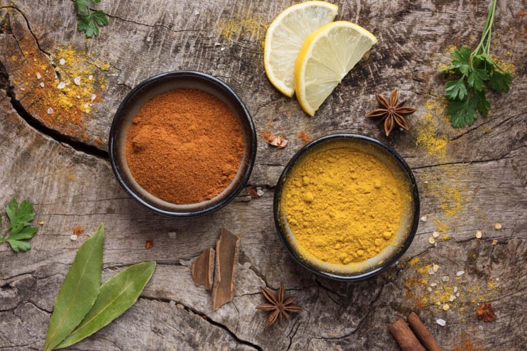 Especiarias usadas para preparar frango ao curry, incluindo curry em pó, folhas de louro, canela e limão, dispostas em um fundo rústico de madeira.

