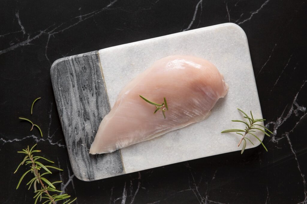 Filé de frango cru com ramos de alecrim sobre uma tábua de mármore.