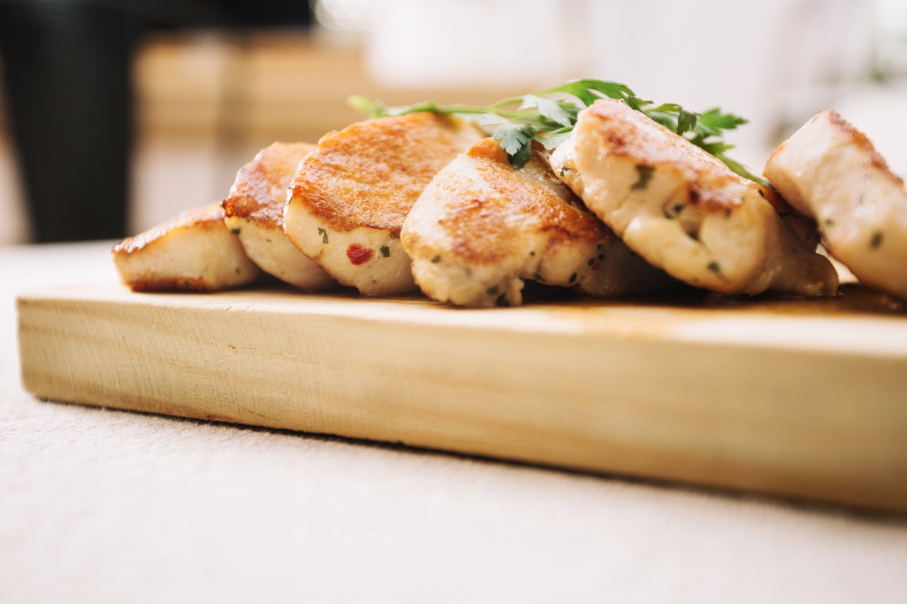 Fatias de frango grelhado temperado para receita de frango xadrez, servido em uma tábua de madeira com ervas frescas.