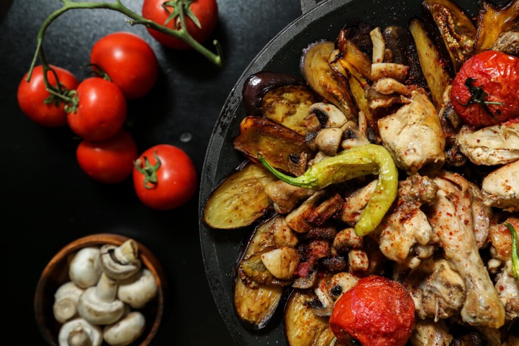 Prato de legumes grelhados na Air Fryer, acompanhado de frango e pimentão, ao lado de tomates frescos e cogumelos, representando uma refeição saudável e saborosa.