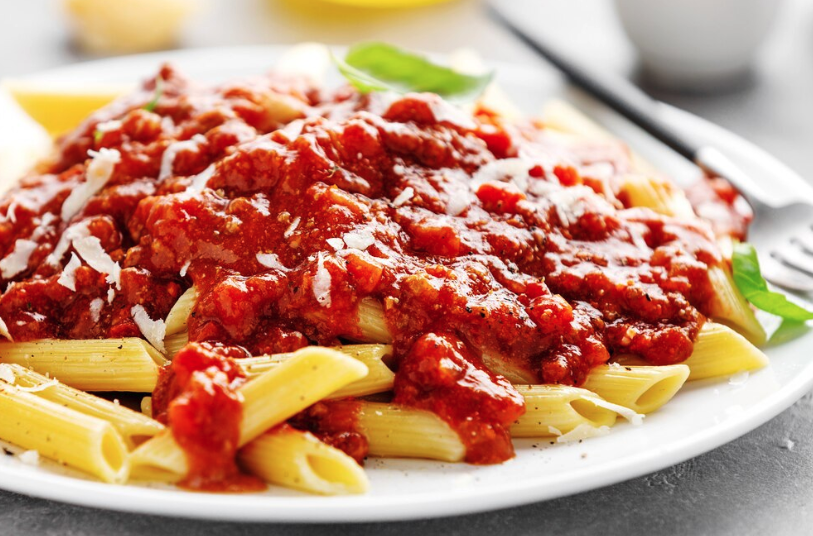 Macarrão penne servido com molho de tomate e carne moída, decorado com folhas de manjericão.