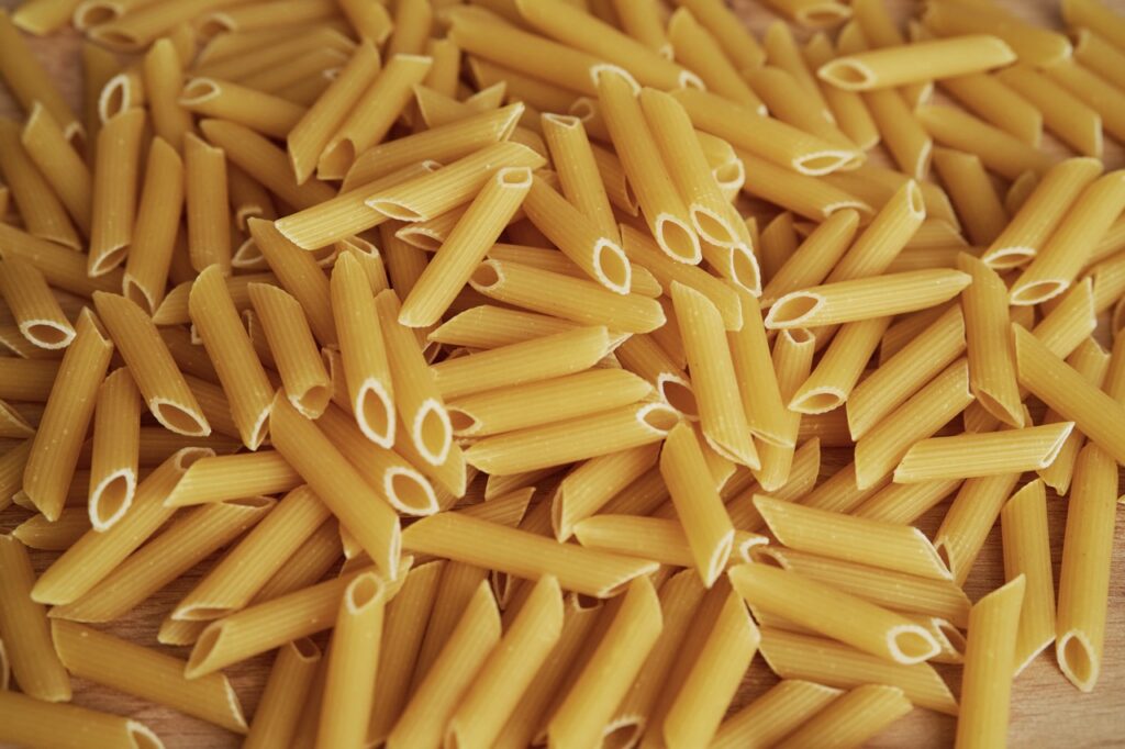 Macarrão penne cru espalhado sobre uma superfície de madeira.