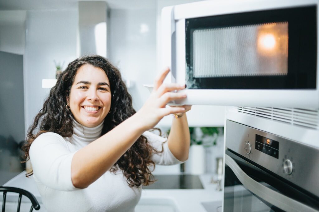 Mulher sorridente usando o micro-ondas em uma cozinha moderna.

