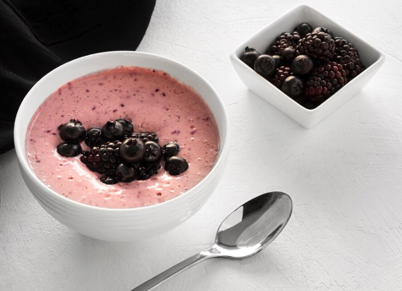Mousse proteica de whey com frutas vermelhas, servida em uma tigela branca e decorada com mirtilos e amoras.