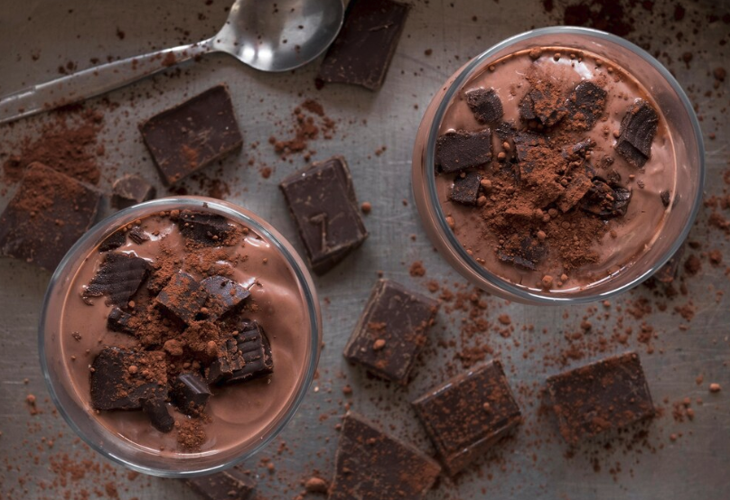 Tigelas de mousse de chocolate proteico com whey, decoradas com pedaços de chocolate e cacau em pó.

