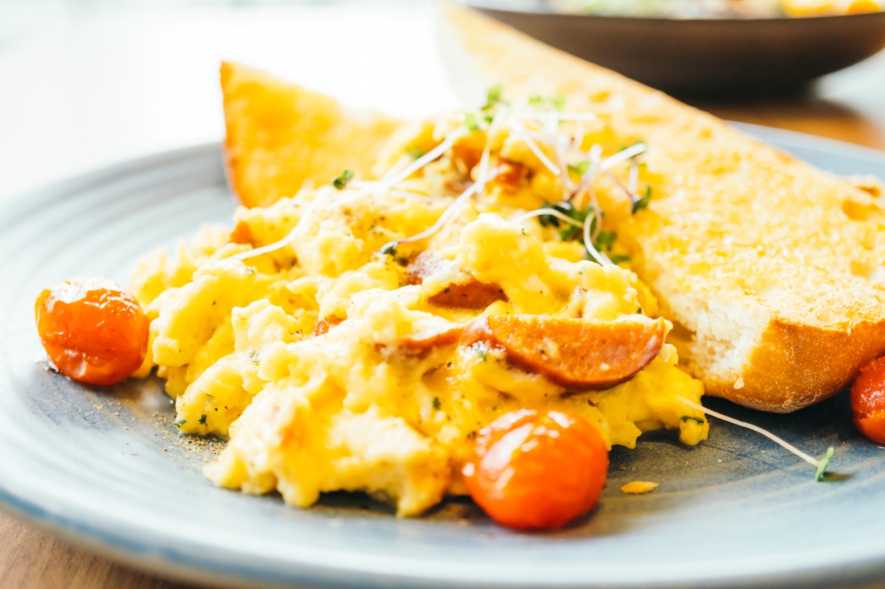 Omelete macia com fatias de linguiça e tomates cereja, acompanhada de torrada dourada.