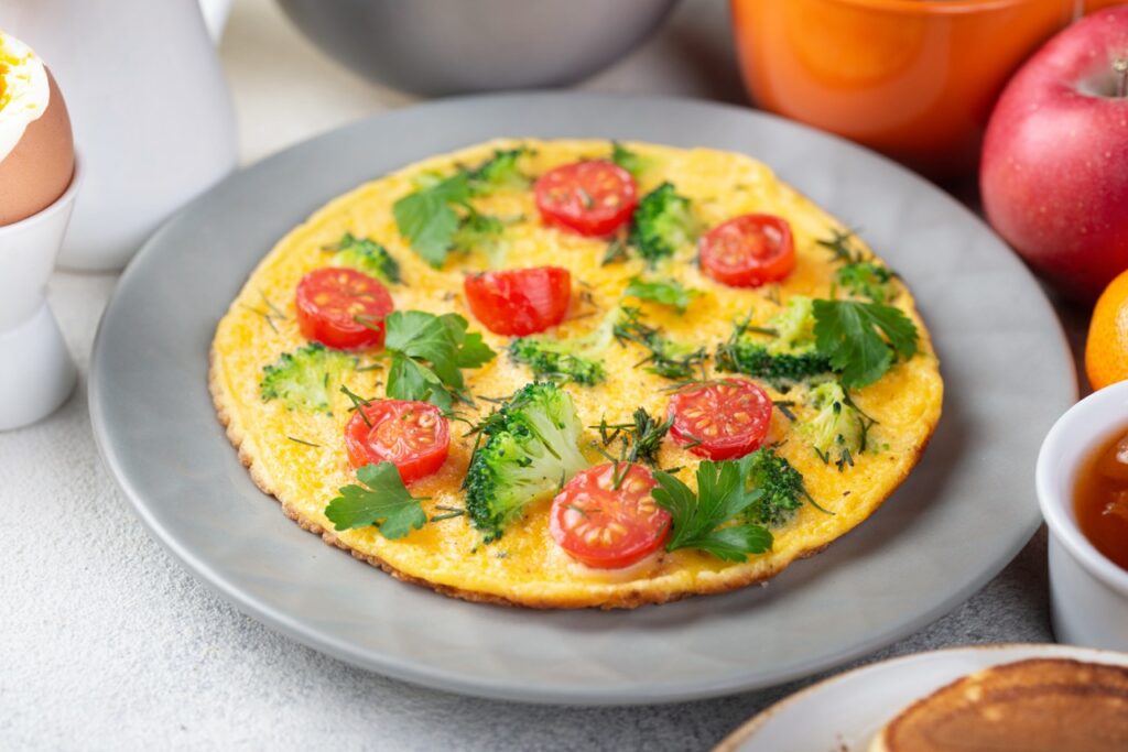 Omelete de micro-ondas pronta, decorada com tomates cereja, brócolis e salsa.

