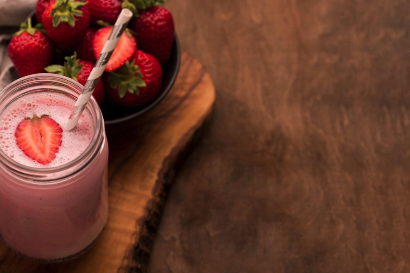 Smoothie de morango com whey, decorado com uma fatia de morango e servido em um pote de vidro com canudo.