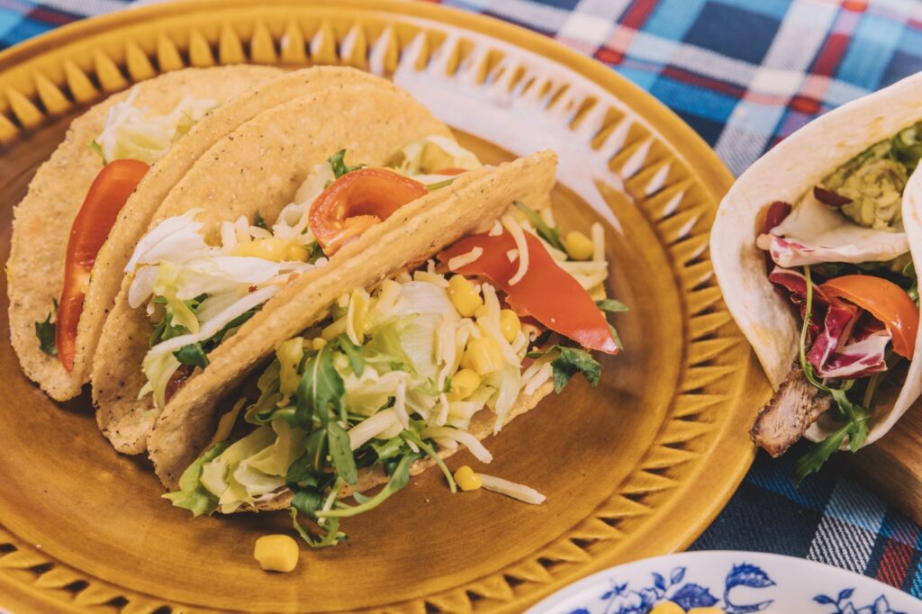Taco recheado com frango desfiado, alface, tomate, milho e queijo, servido em um prato rústico, ideal para uma refeição saborosa e prática.