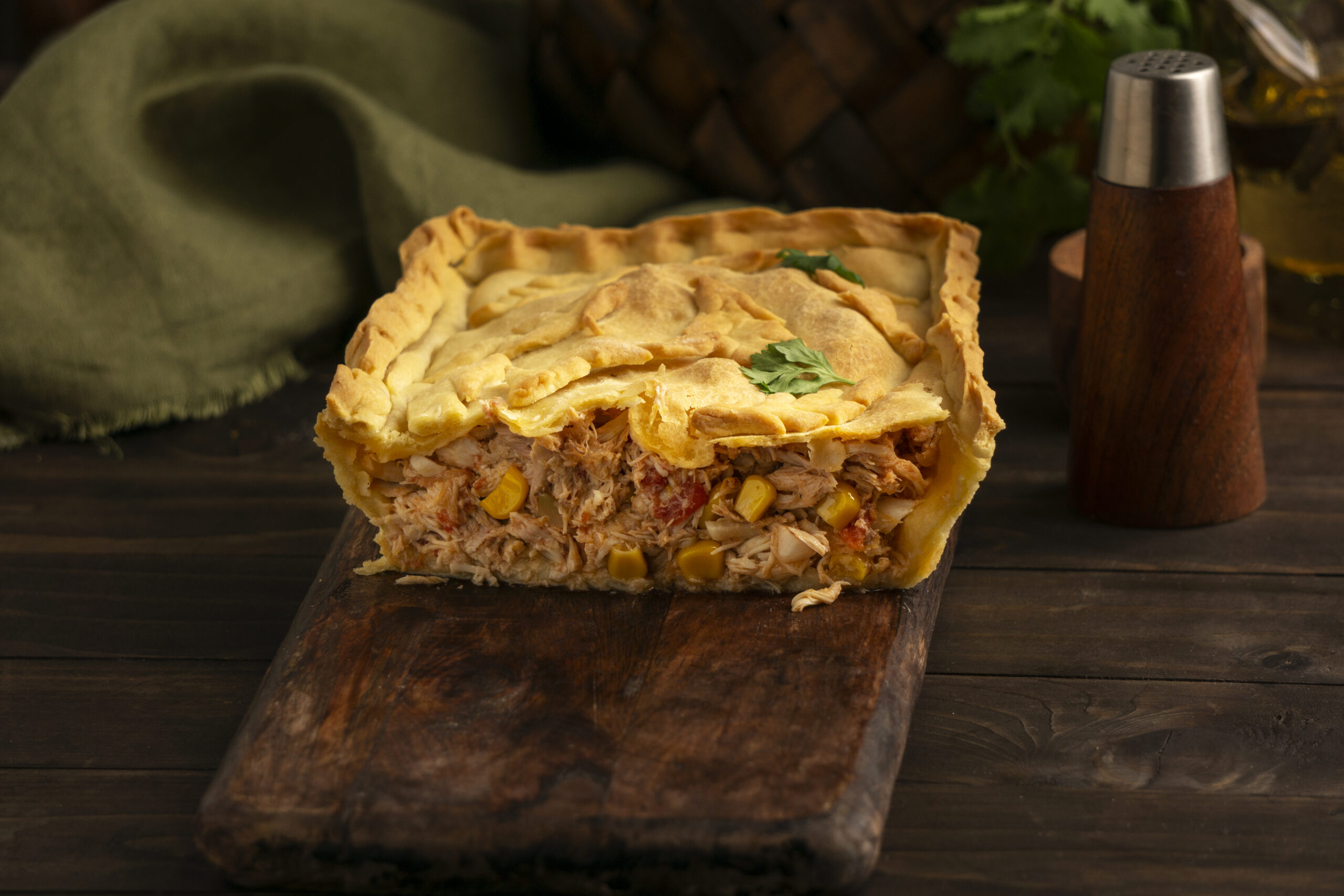 Torta salgada de liquidificador fácil com recheio de frango e milho sobre uma tábua de madeira.