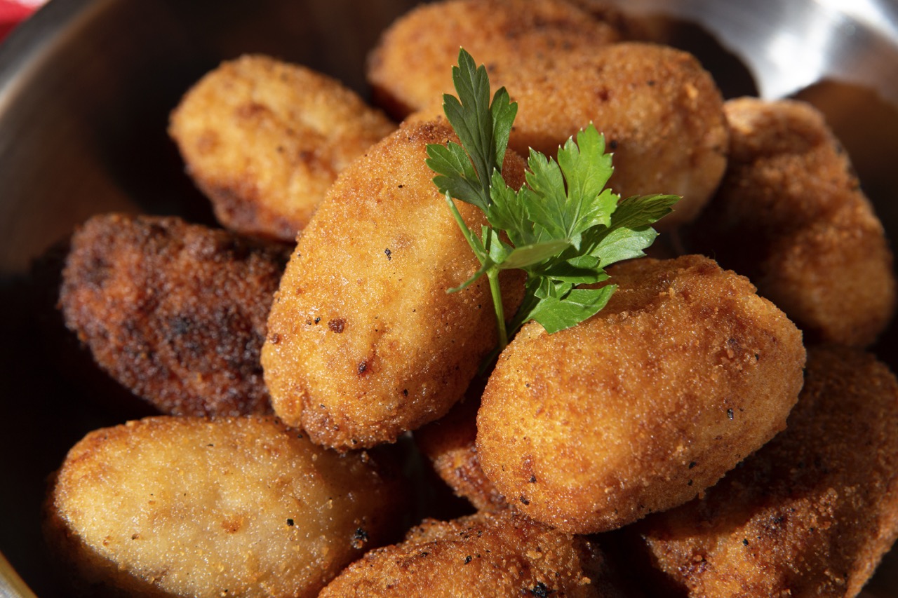 Prato de croquetes dourados e crocantes servidos com um toque de salsa fresca no topo, perfeitos para um lanche ou aperitivo delicioso.