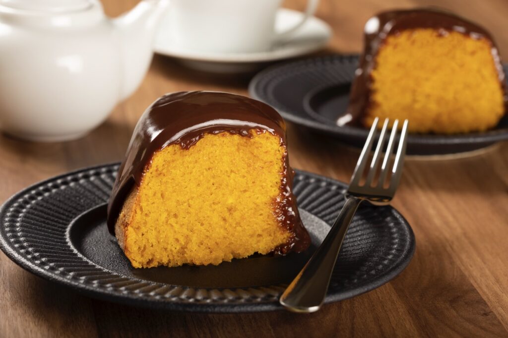 Bolo de cenoura fofinho com cobertura de chocolate cremoso servido em prato preto.