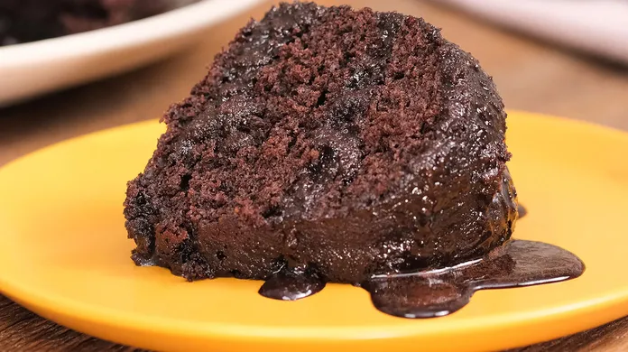 Fatia de bolo de chocolate fofinho e molhadinho com calda, servida em prato amarelo.