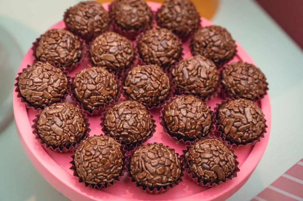 Brigadeiros prontos, cobertos com granulado de chocolate e servidos em uma bandeja rosa.