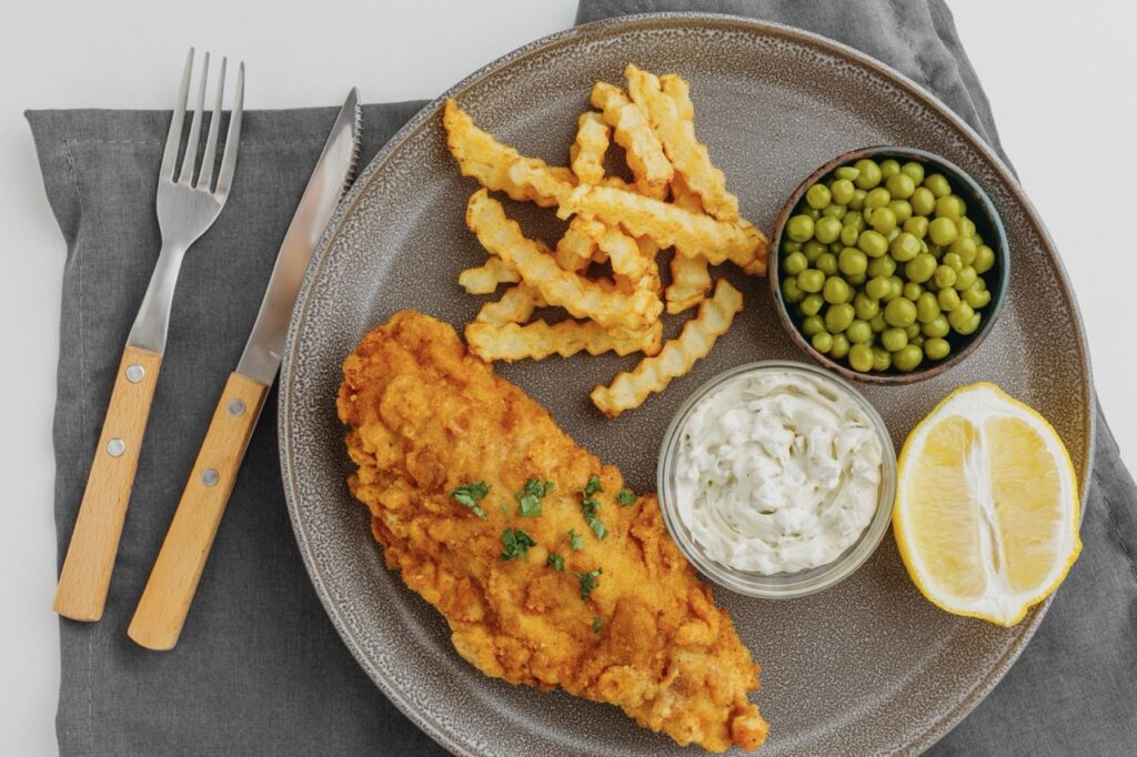Prato com peixe empanado crocante preparado na Air Fryer, acompanhado de batatas fritas, ervilhas e molho cremoso, ideal para uma refeição leve e saudável.