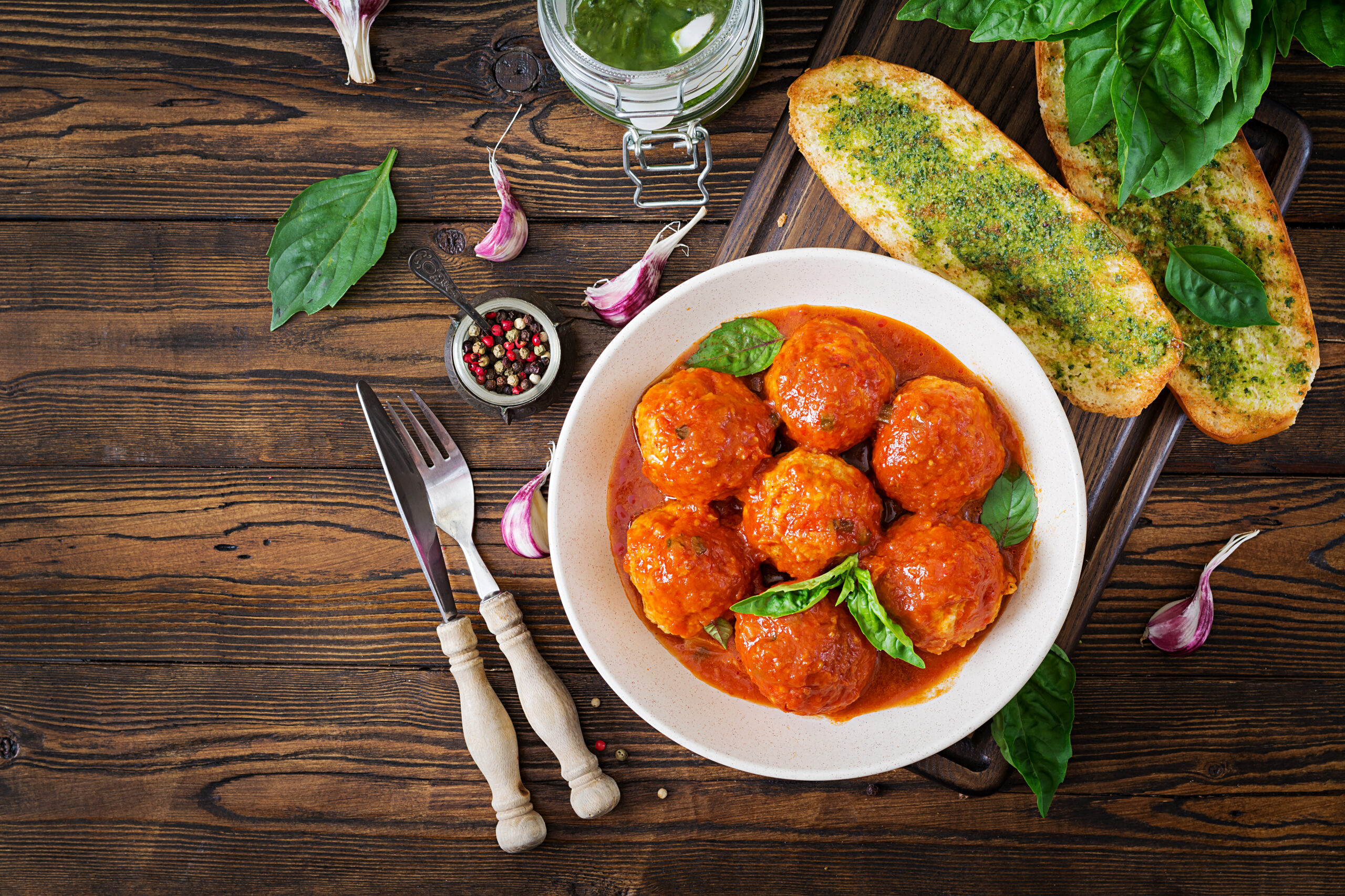 Almôndegas de grão-de-bico com molho de tomate servidas em um prato branco com folhas de manjericão fresco, acompanhadas de pão com ervas e alho.