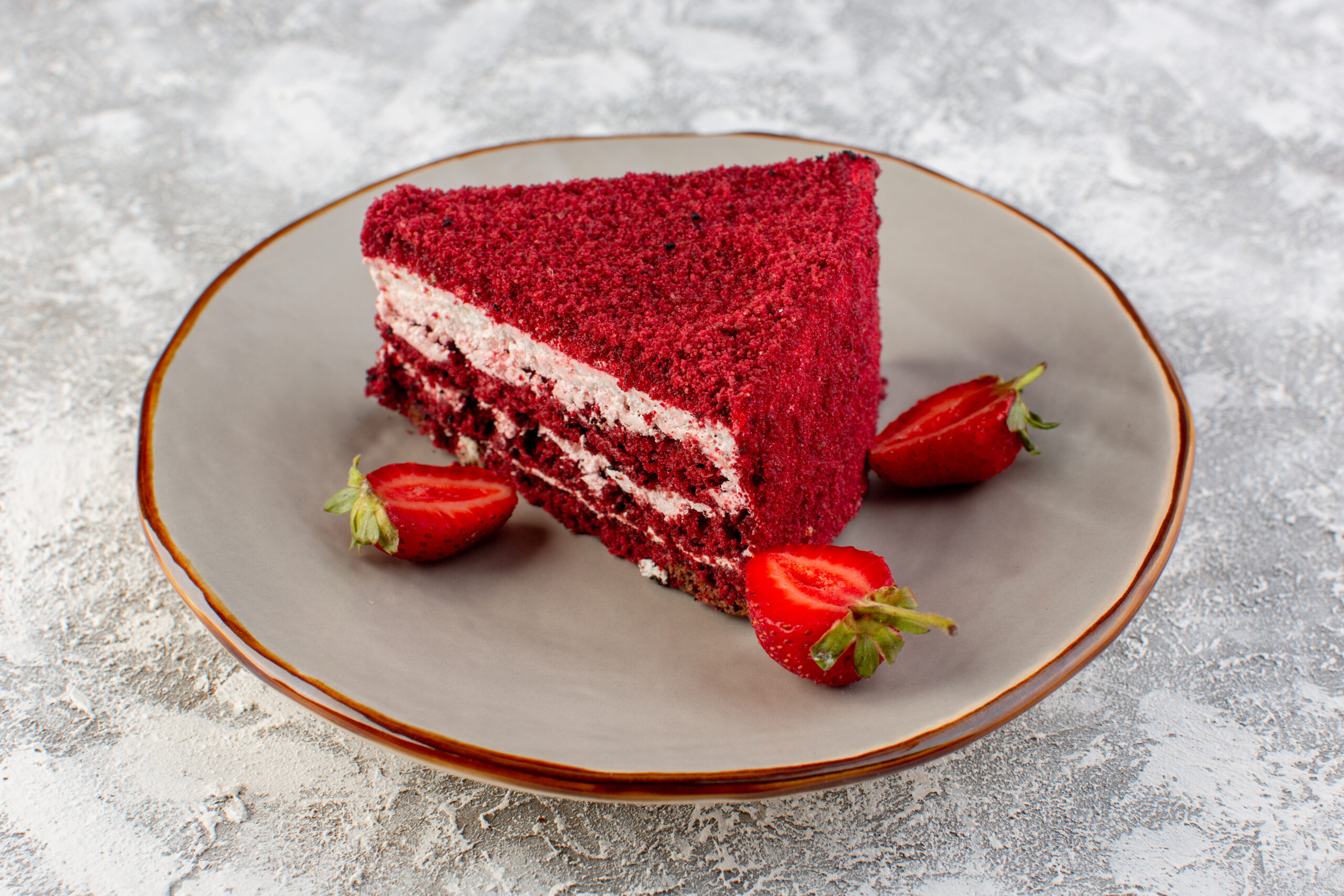 Fatia de bolo red velvet proteico com whey, decorada com morangos frescos em um prato cinza.