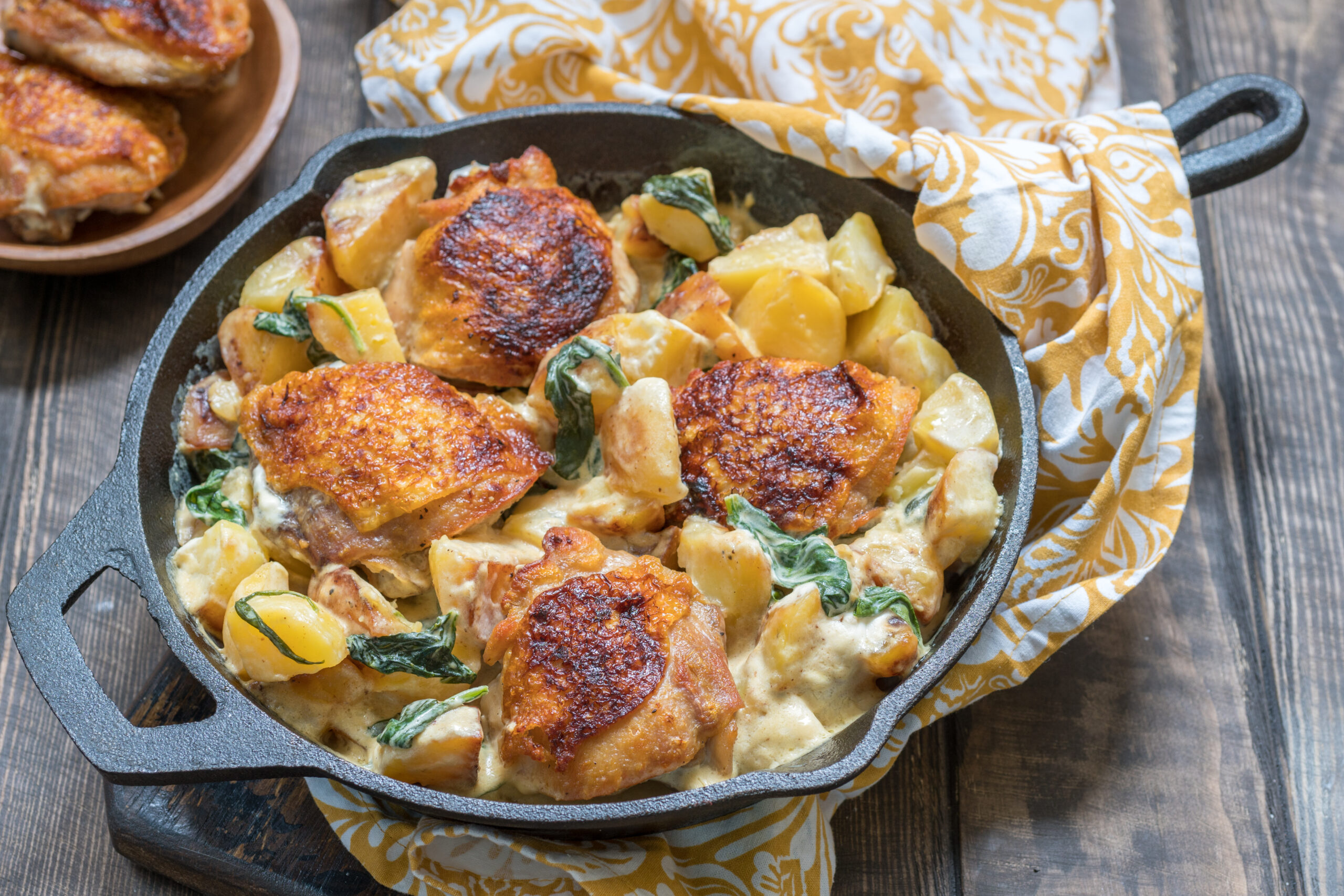 Frango ao molho de queijo e ervas finas no forno servido com batatas douradas e espinafre em uma frigideira rústica.