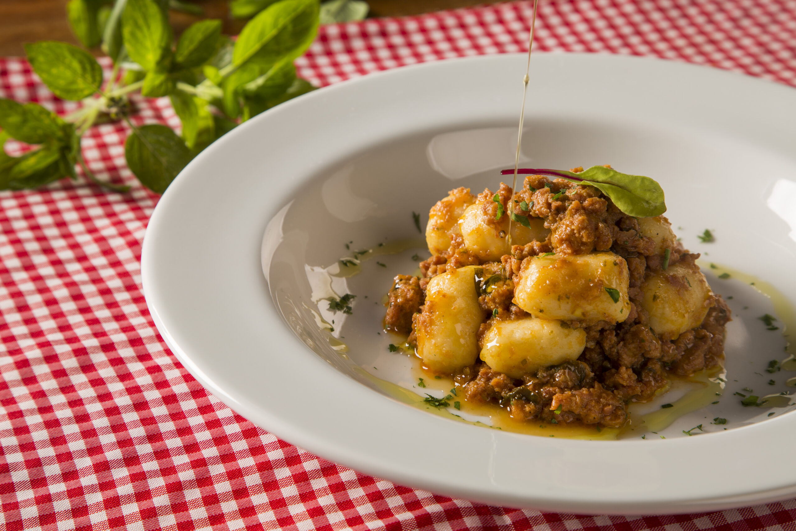 Nhoque de batata com molho bolonhesa servido em prato fundo com decoração de ervas frescas.