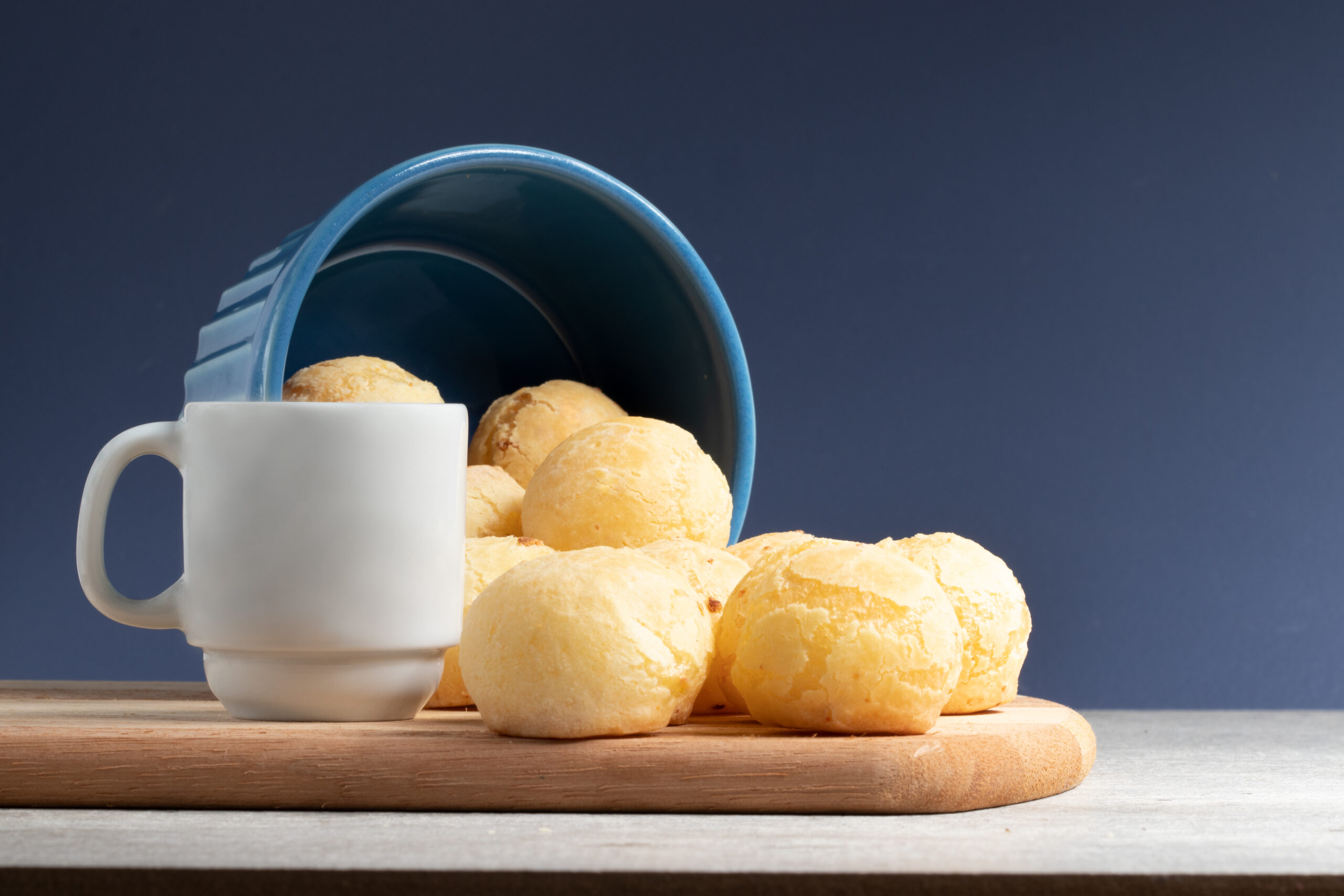 Pão de queijo de caneca acompanhado de caneca branca sobre uma tábua de madeira.