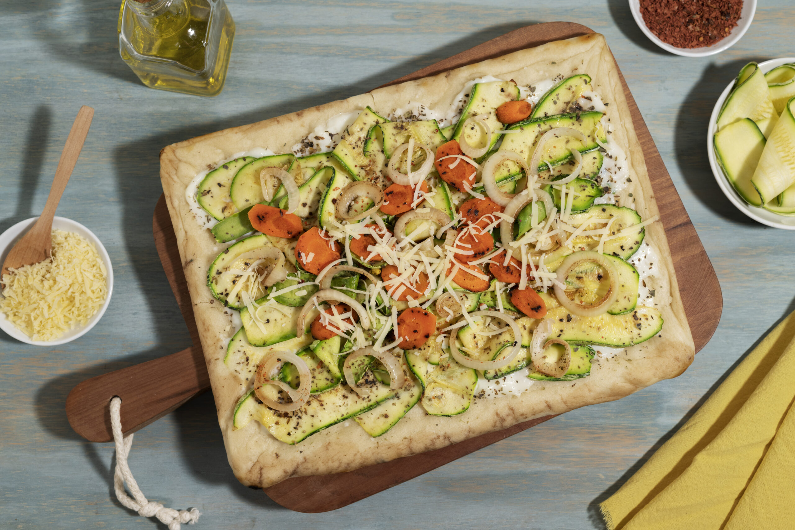 Pizza fitness com massa de couve-flor coberta com vegetais frescos como abobrinha, cenoura e cebola, finalizada com queijo ralado.
