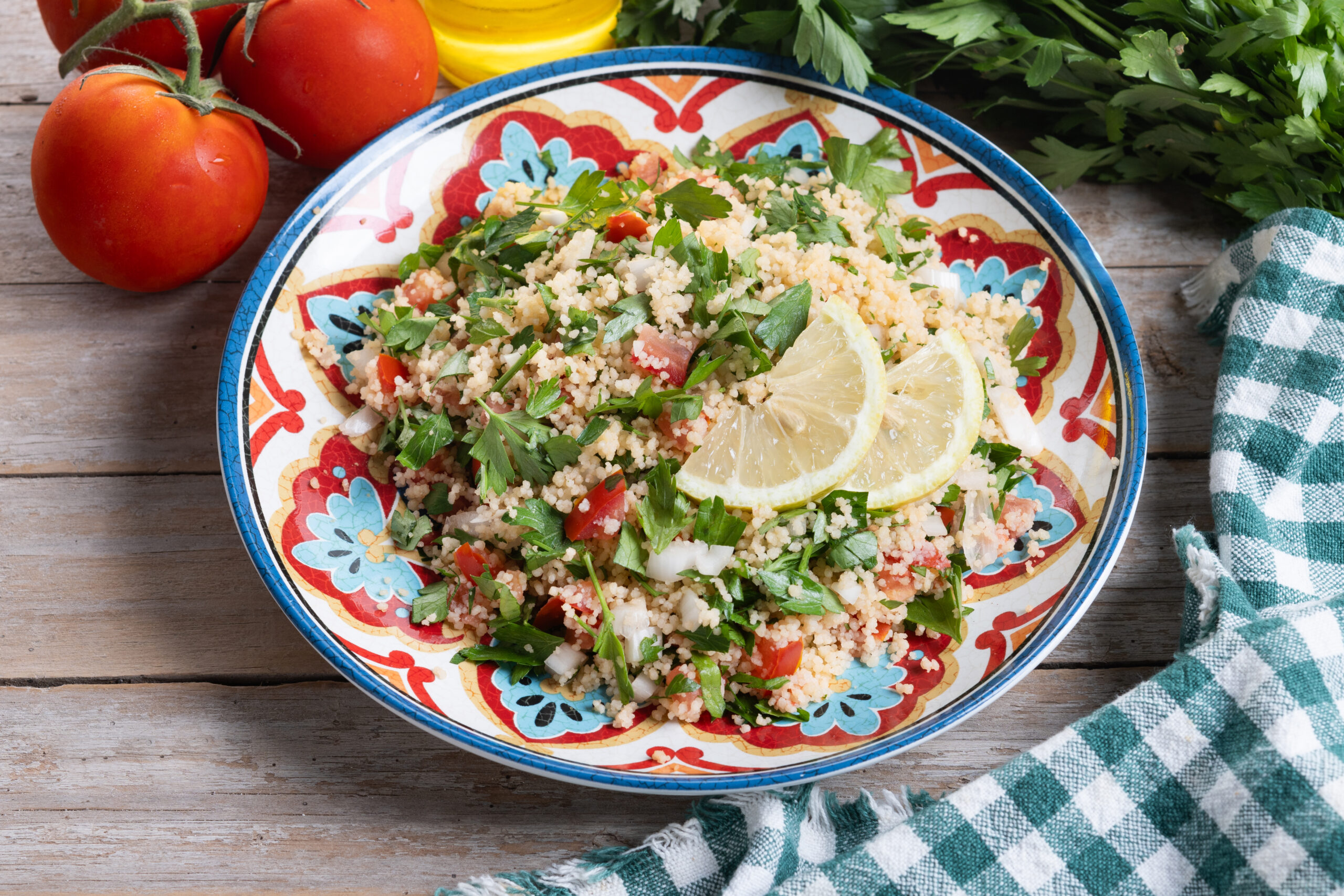 Prato de tabule de bulgur com grão-de-bico e ervas frescas, servido em um prato colorido, decorado com fatias de limão e acompanhado por tomates frescos ao fundo.