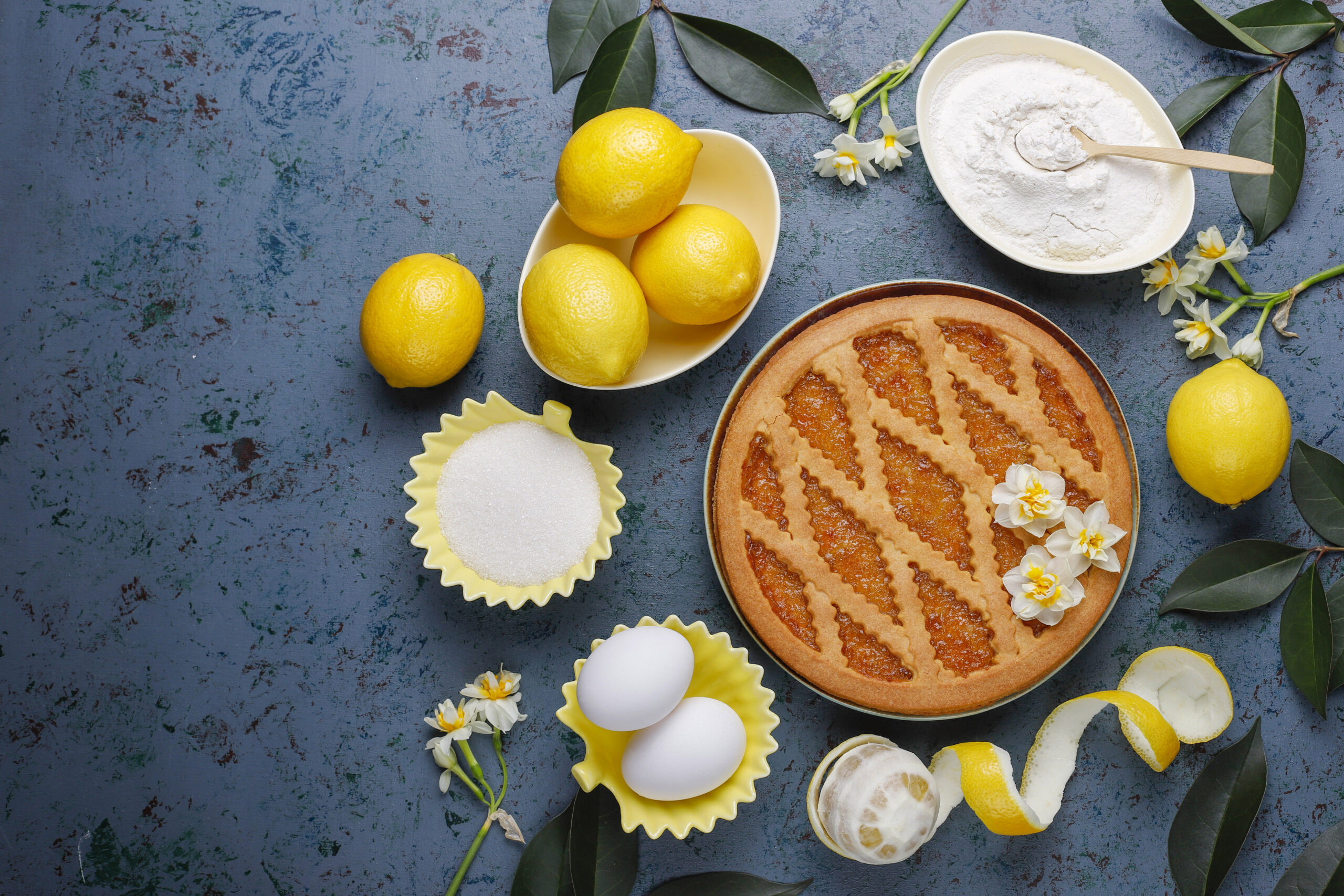 Torta de limão low carb com massa de amêndoas, rodeada por ingredientes frescos como limões, ovos e farinha, em um fundo rústico decorado.