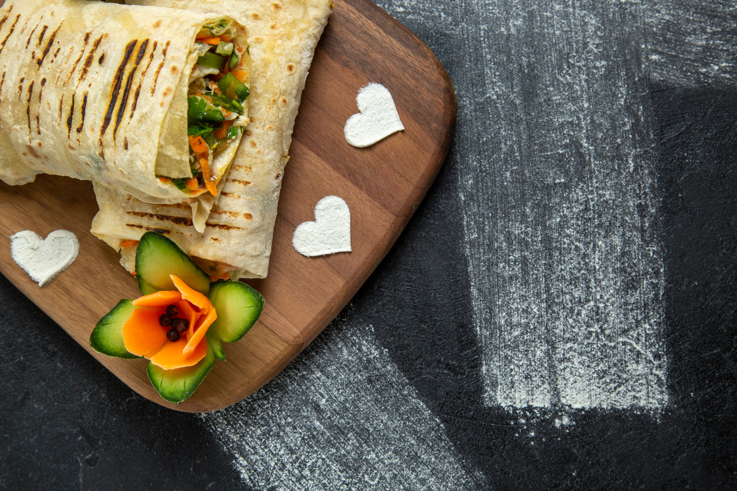 Wrap de frango com creme de abacate em tábua de madeira, decorado com flores de legumes.