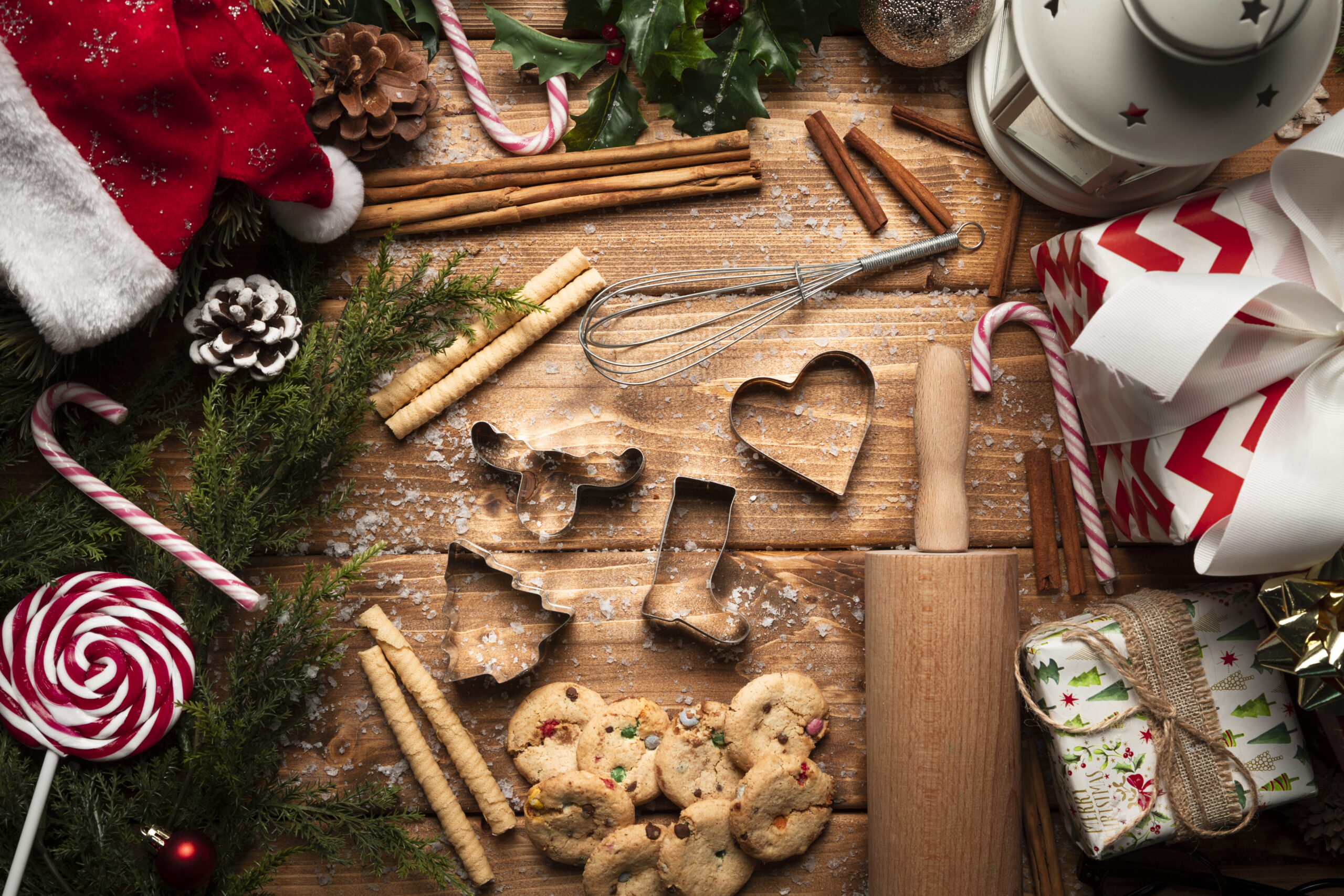 Decoração natalina com cortadores de biscoito, bengalas doces, presentes e ingredientes para receitas natalinas em uma mesa de madeira.