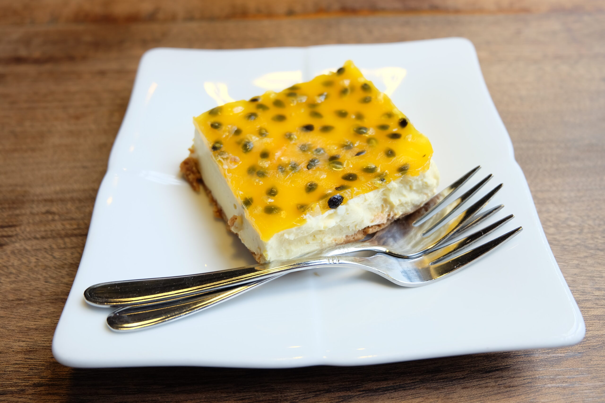 Fatia de bolo de maracujá com cobertura de ganache de chocolate branco em prato branco, decorada com sementes de maracujá.