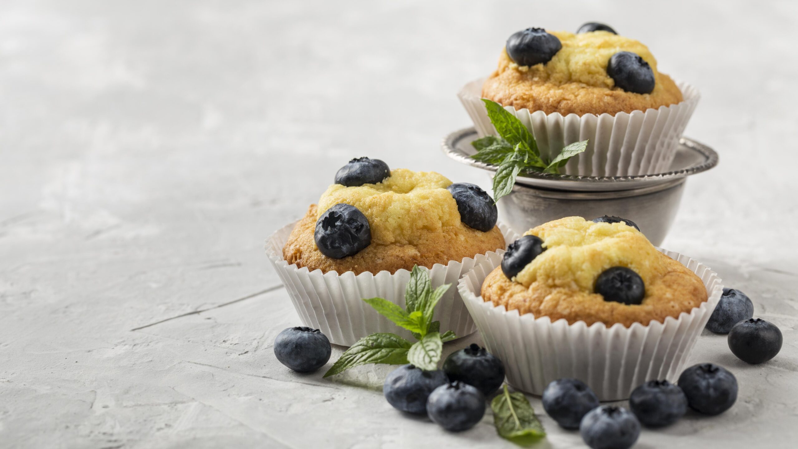 Muffins proteicos de blueberry com whey decorados com folhas de hortelã em um fundo cinza claro.