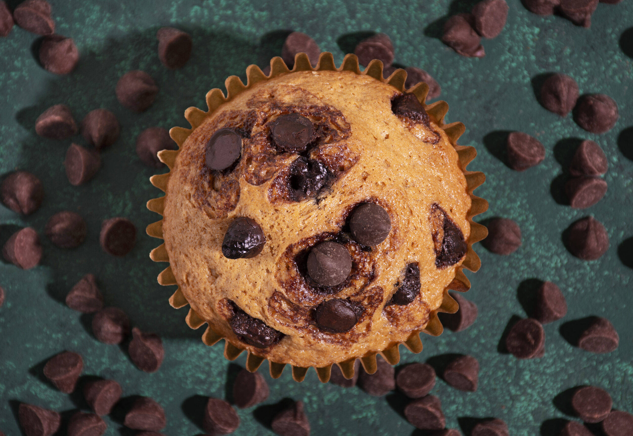 Muffin de amêndoas low carb com gotas de chocolate 70% cacau, em fundo verde decorado com pedaços de chocolate.