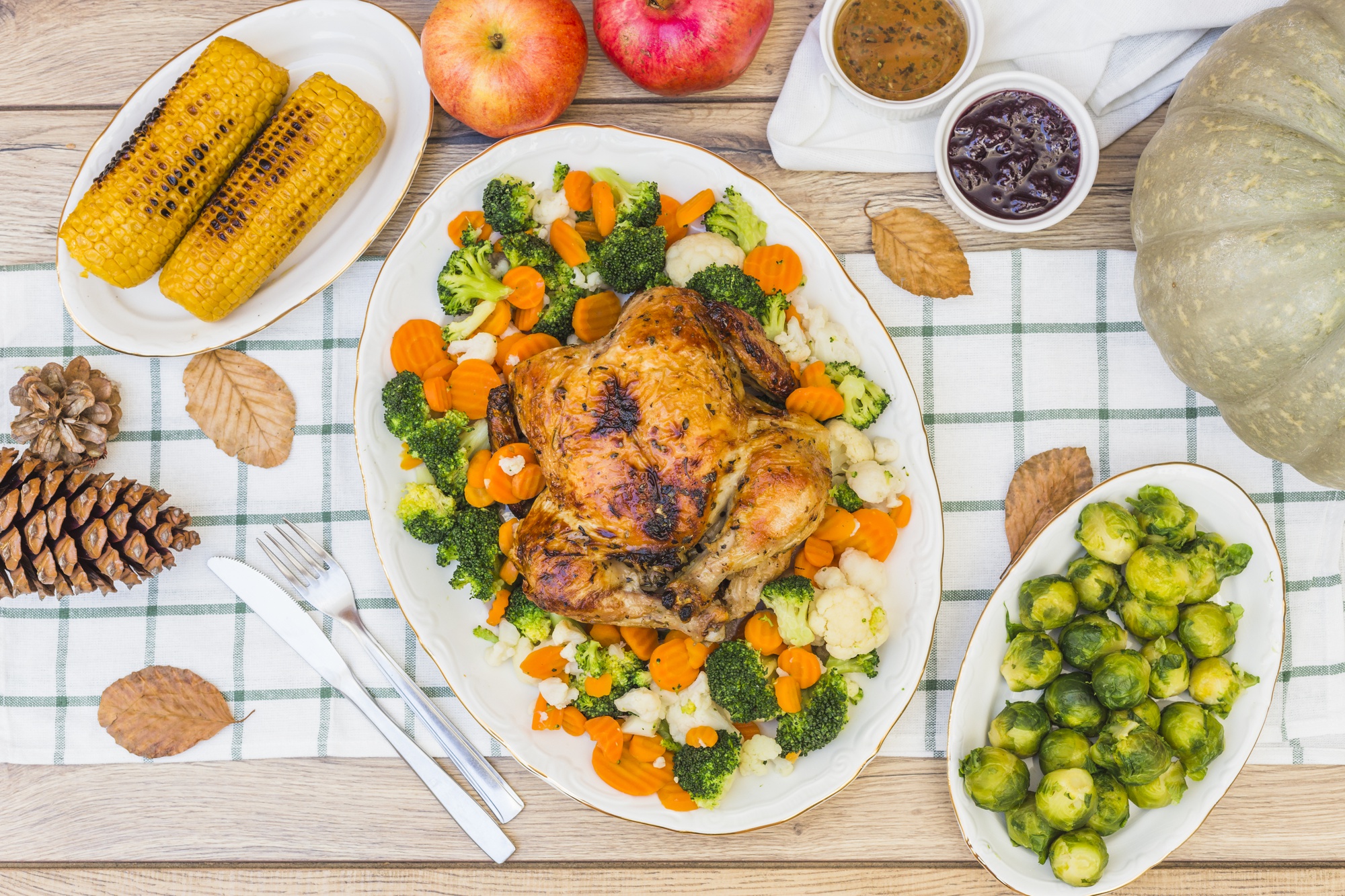 Frango assado com legumes servido em uma mesa decorada com milho, couve-de-bruxelas e acompanhamentos.