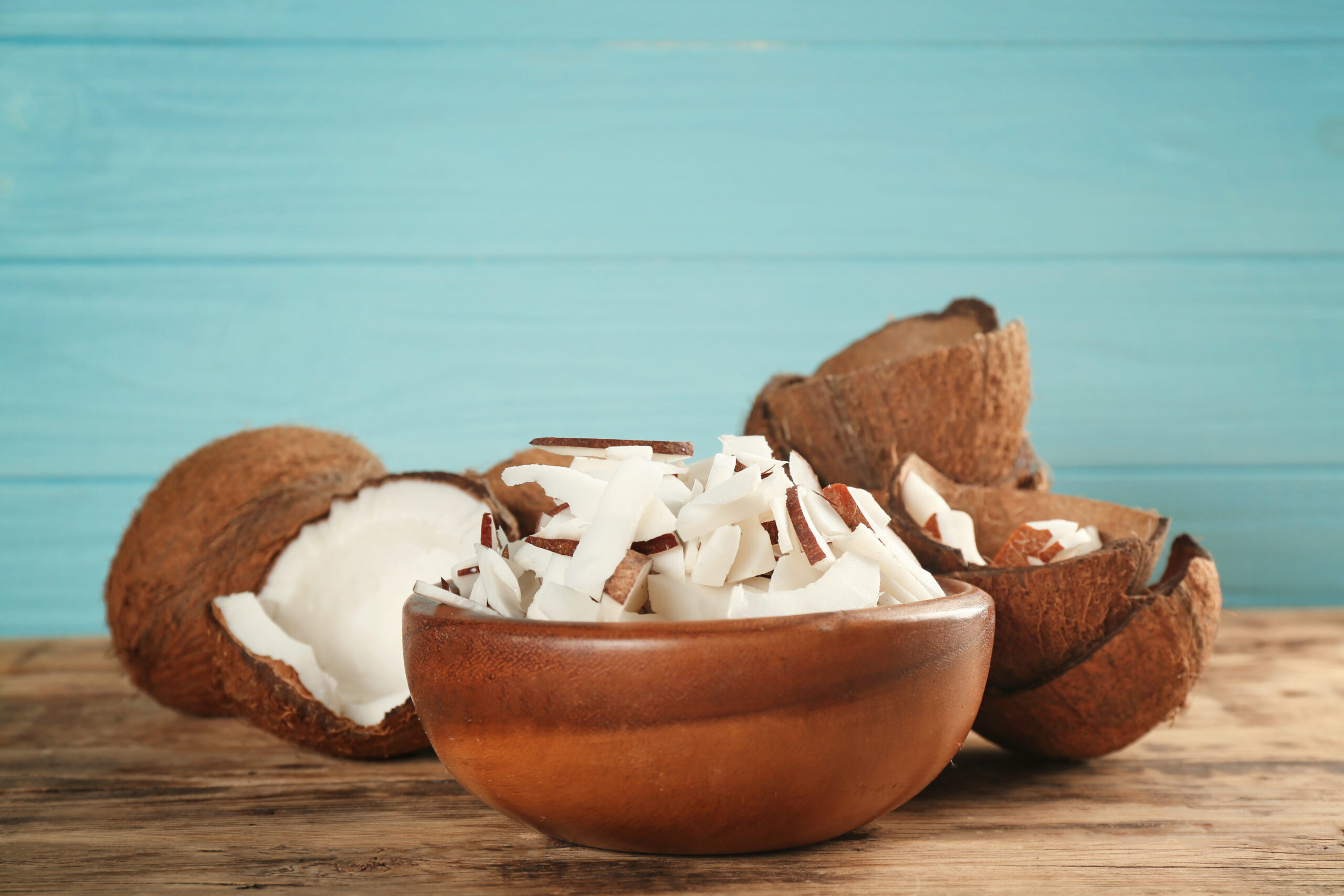 Coco fresco em lascas em tigela de madeira com cascas ao fundo