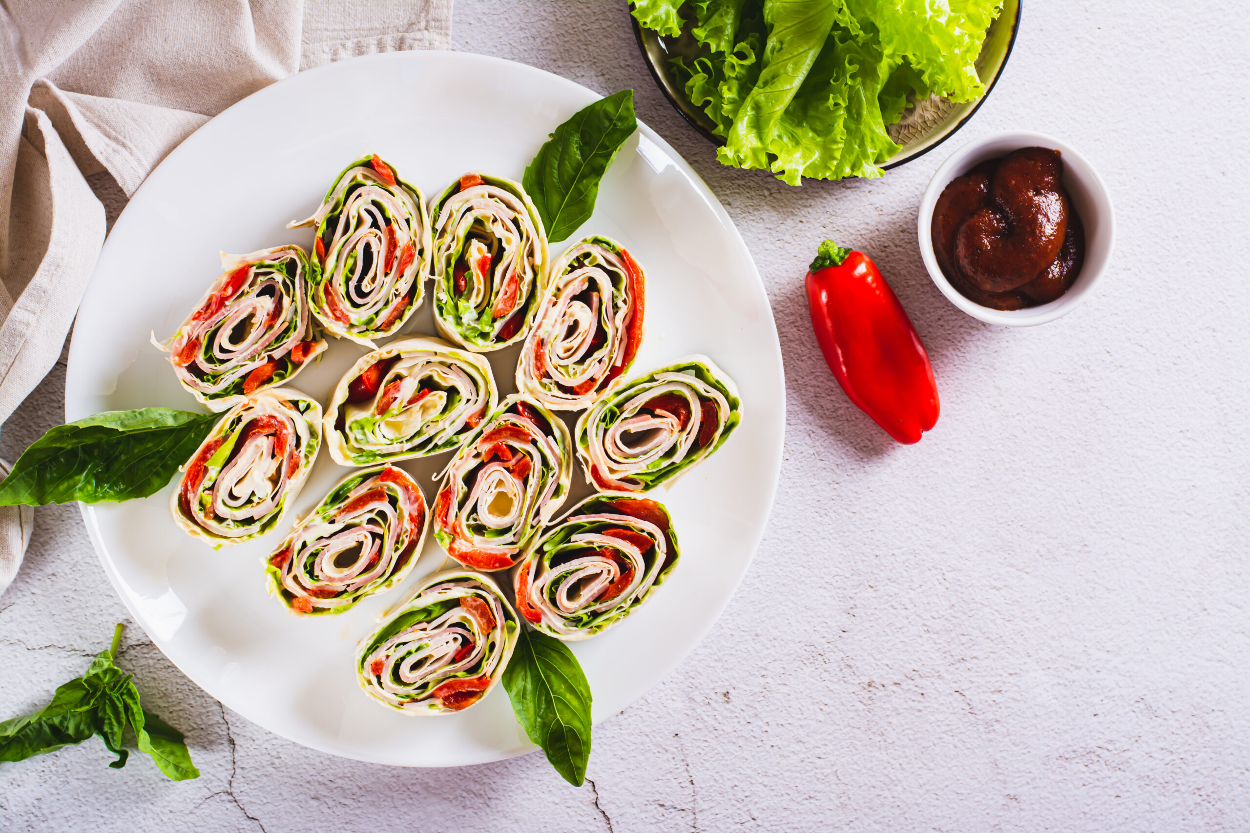 Wrap integral de peito de peru com alface e iogurte servido em um prato branco, decorado com folhas de manjericão e acompanhado de alface e molho.